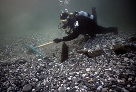 Taucher bedeckt mit einem Rechen und Pfahlstummel am Seeboden