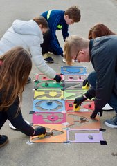 Kinder malen mit Straßenkreide große bunte Buchstabenschablonen aus